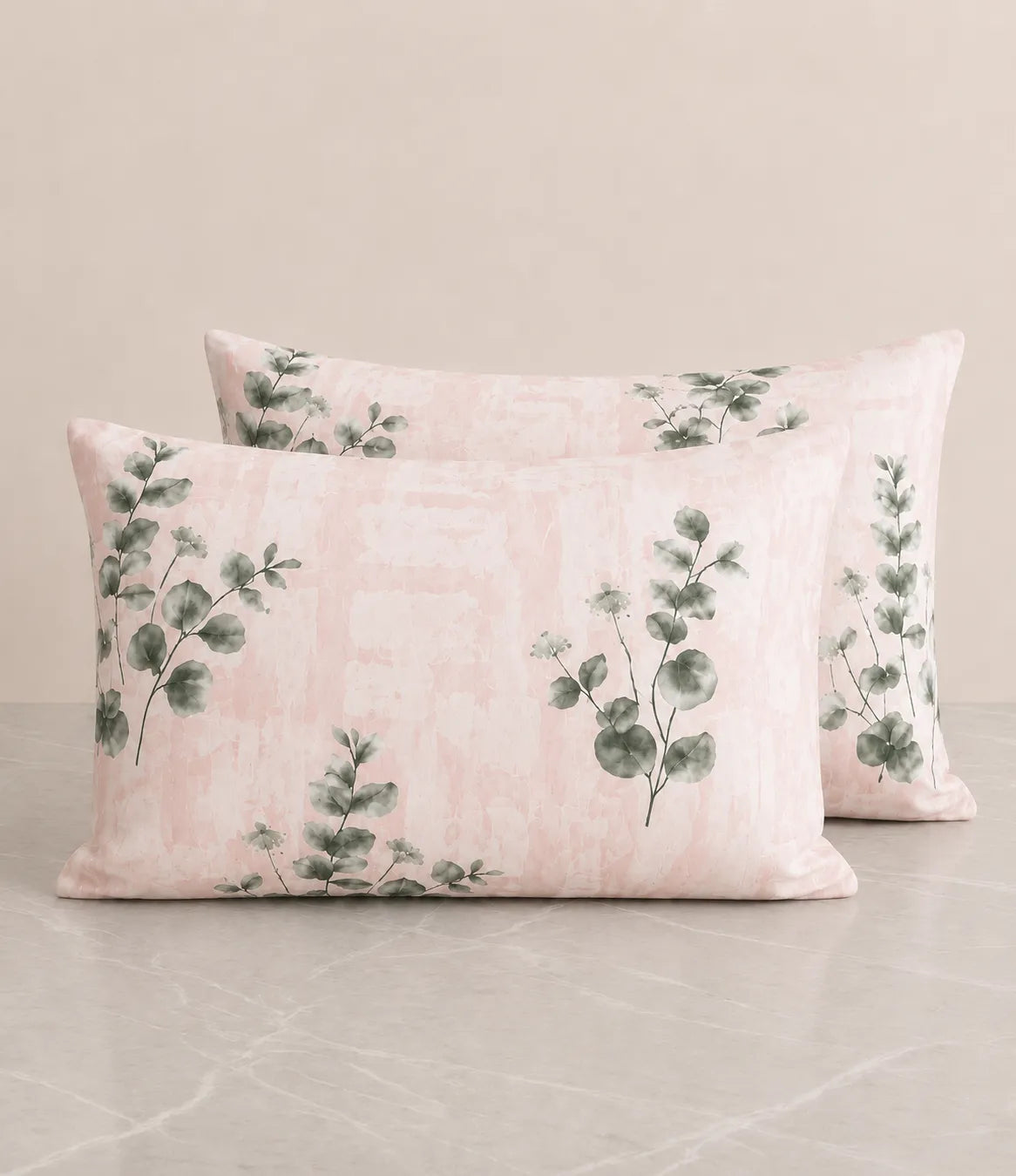Set of blush pink pillow covers with watercolor eucalyptus leaf print on a soft textured background.
