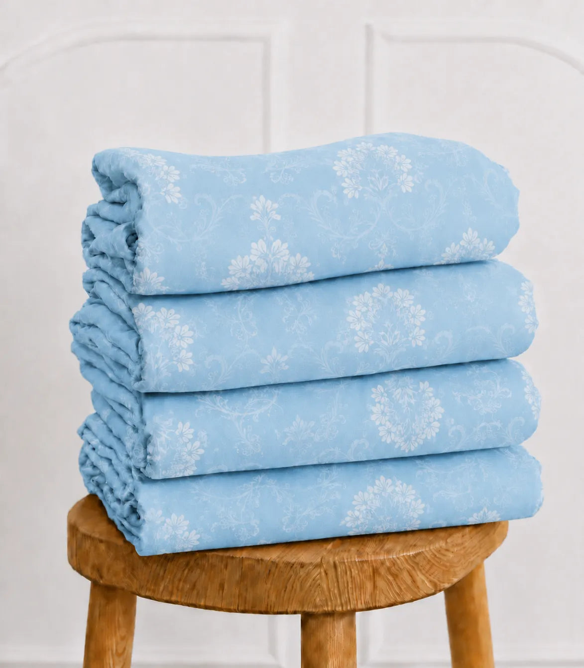 Folded king size sky blue cotton bedsheet set with elegant white floral vine design, showcasing soft fabric and premium craftsmanship.