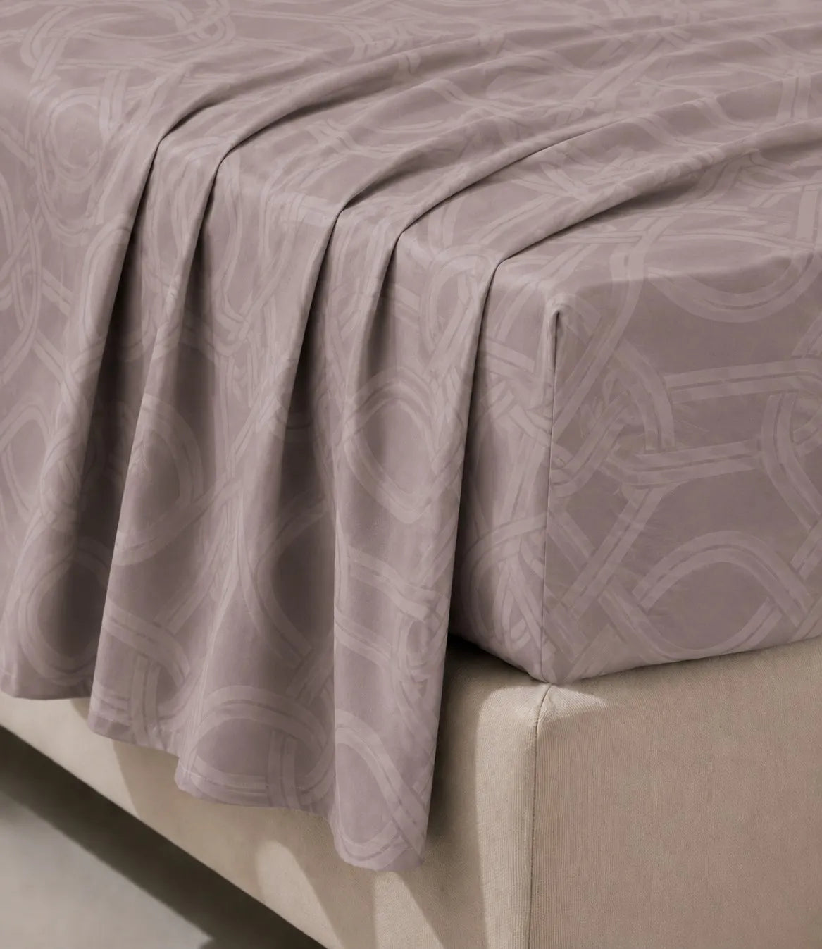 Close-up of blush mauve cotton bedsheet fabric showing soft texture, elegant drape, and interwoven geometric pattern.