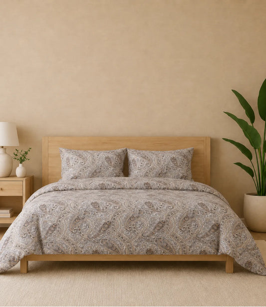 Premium queen size 100% pure cotton bedsheet featuring an elegant beige paisley print with intricate traditional motifs in warm brown, grey, and ivory tones, beautifully styled in a modern wooden bedroom with matching pillow covers for a timeless and luxurious sleeping experience.