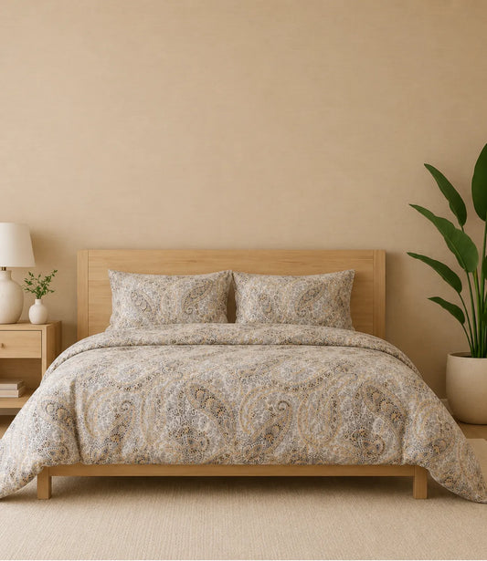 Premium queen size 100% pure cotton bedsheet featuring an elegant ivory paisley print with intricate heritage-inspired motifs in beige, gold, grey, and brown tones, beautifully styled in a modern wooden bedroom with matching pillow covers for a timeless and luxurious sleeping experience.