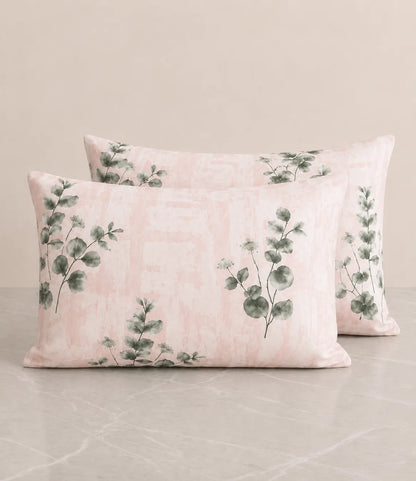 Set of blush pink pillow covers with watercolor eucalyptus leaf print on a soft textured background.