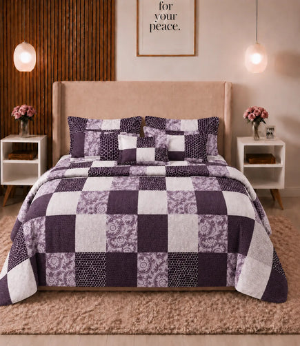 Front view of a queen-size cotton bedsheet set featuring a contemporary patchwork design in plum, lavender, and white with floral, textured, and geometric square patterns. The bed is styled with matching pillow covers in a modern bedroom.
