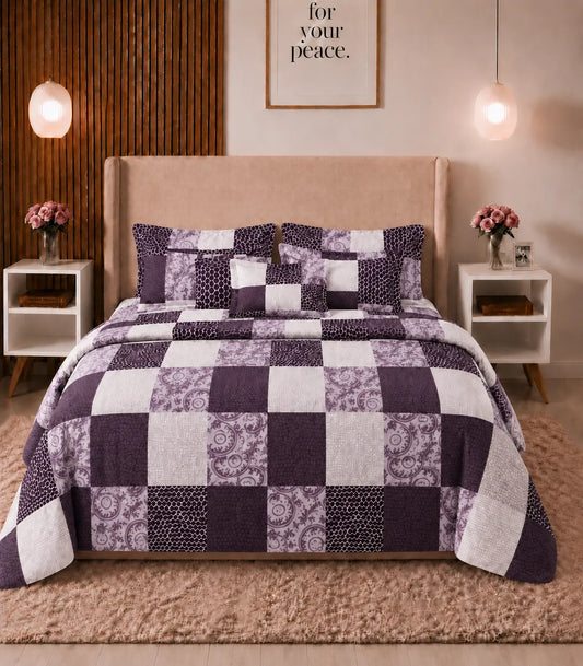 Front view of a queen-size cotton bedsheet set featuring a contemporary patchwork design in plum, lavender, and white with floral, textured, and geometric square patterns. The bed is styled with matching pillow covers in a modern bedroom.