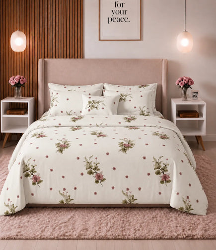 Queen-size cotton bedsheet set with a soft ivory base, pink floral bouquets, green leafy accents, and scattered tiny blossoms, neatly styled on a modern upholstered bed in a warm, elegant bedroom.