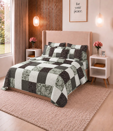 Angled view of a queen size cotton bedsheet featuring a geometric patchwork print in black, grey, sage green, and white, paired with coordinated pillow covers in a stylish bedroom setting.