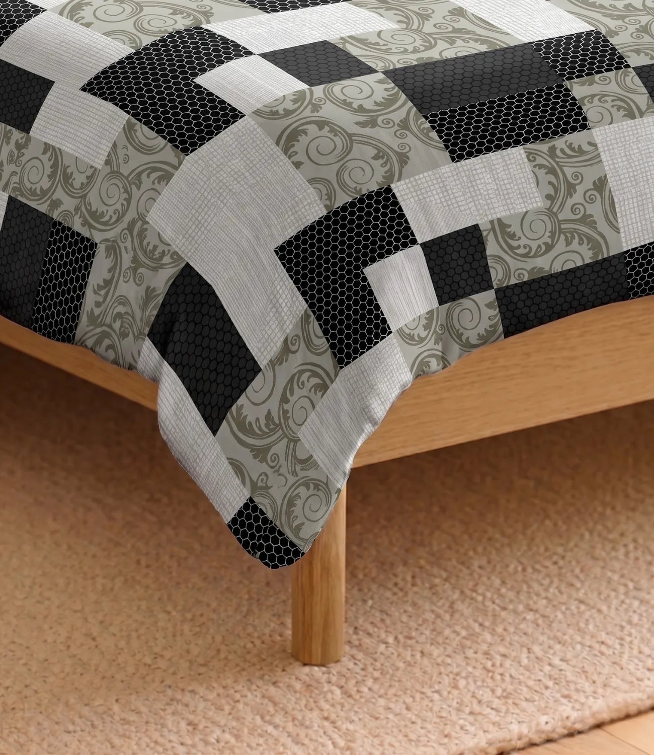 Close-up of the queen size cotton bedsheet draped over a bed corner, highlighting the contemporary patchwork print in black, grey, sage green, and white with a smooth fabric finish.