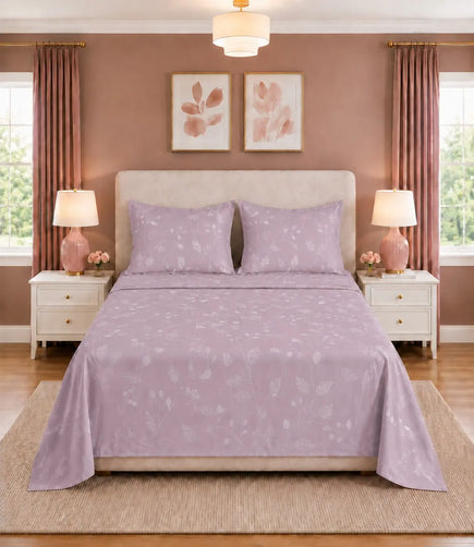 Front-facing view of a blush lavender botanical print king-size cotton bedsheet with matching pillow covers, beautifully arranged on a contemporary bed between white bedside tables with pink lamps in a cozy bedroom.