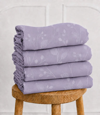 Folded lavender botanical vine cotton bedsheet set neatly stacked on a wooden stool, showcasing the soft fabric and delicate leaf pattern.