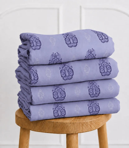 Folded lavender king size cotton bedsheet set with decorative medallion pattern neatly stacked on a wooden stool, showcasing premium cotton fabric and fine craftsmanship.
