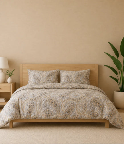Premium queen size 100% pure cotton bedsheet featuring an elegant ivory paisley print with intricate heritage-inspired motifs in beige, gold, grey, and brown tones, beautifully styled in a modern wooden bedroom with matching pillow covers for a timeless and luxurious sleeping experience.
