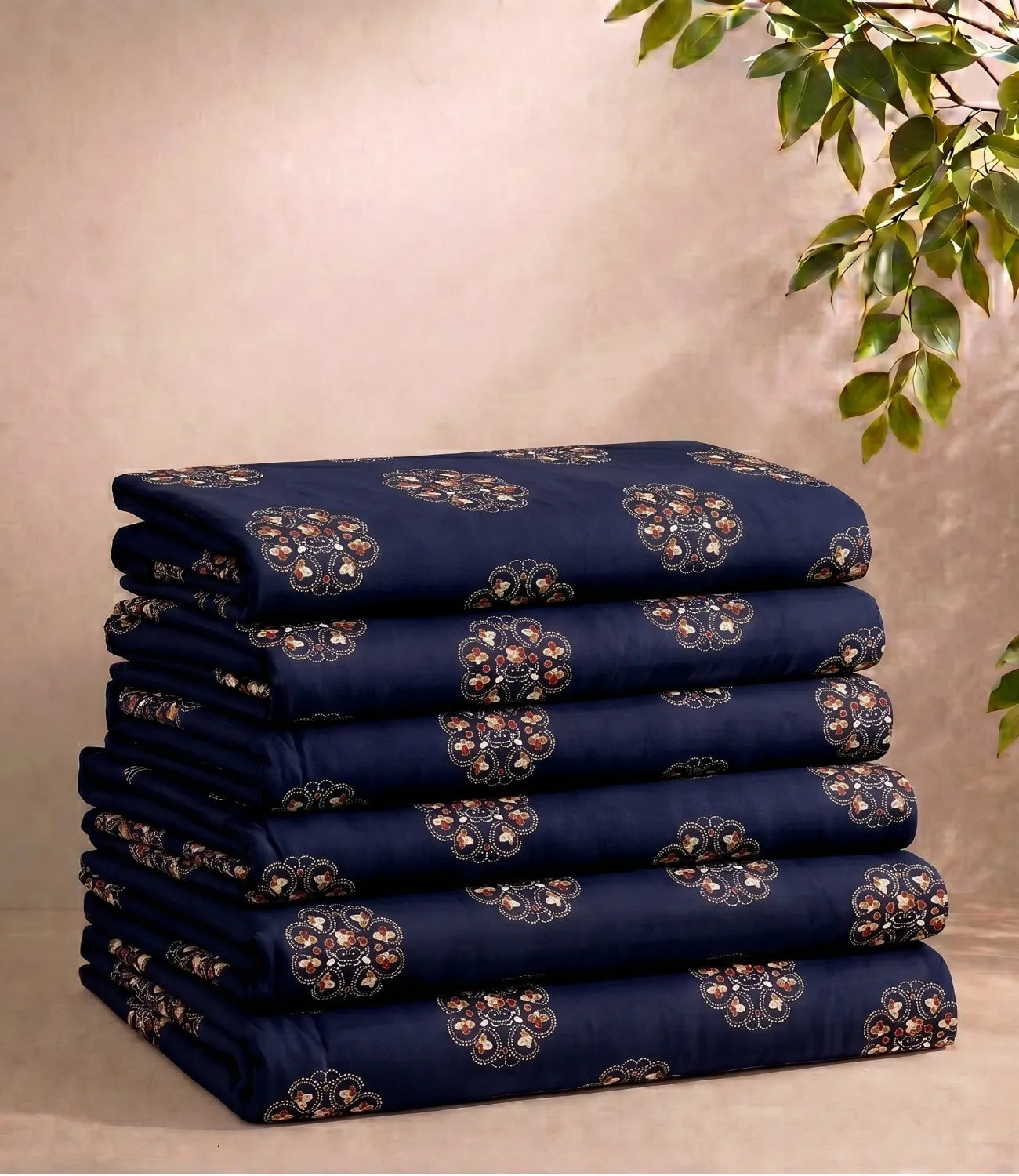 Neatly folded queen size cotton bedsheet set in midnight navy with repeating floral medallion motifs. The stack displays the fabric's quality and coordinated print against a soft neutral backdrop with decorative greenery.