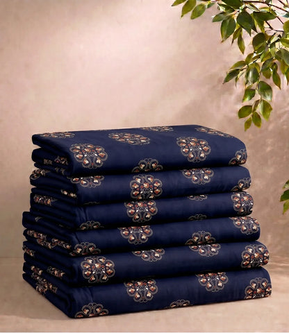 Neatly folded queen size cotton bedsheet set in midnight navy with repeating floral medallion motifs. The stack displays the fabric's quality and coordinated print against a soft neutral backdrop with decorative greenery.