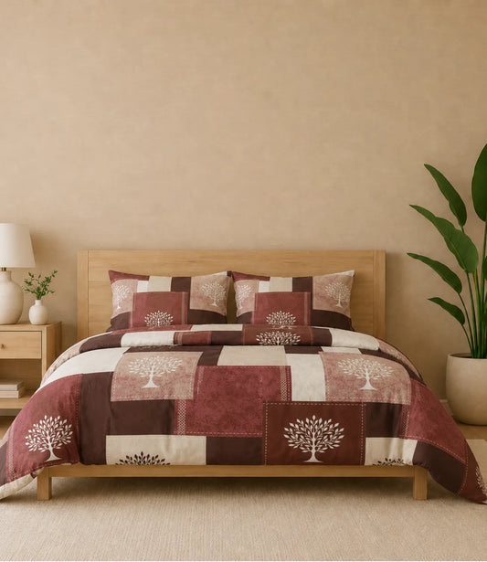 Queen-size cotton bedsheet set featuring a rustic patchwork design in maroon, brown, beige, and cream with elegant white tree motifs. Displayed on a wooden bed with two matching pillow covers in a warm, modern bedroom setting.