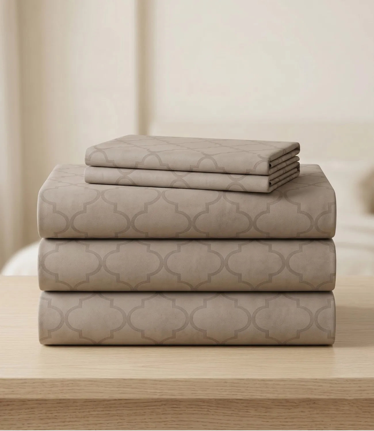 Neatly folded beige geometric bedsheet set stacked on a wooden table, displaying the coordinated flat sheet, fitted sheet, and pillow covers with a modern printed design.