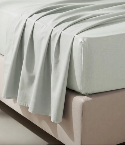 Close-up of a mint green king size fitted cotton bedsheet draped over a mattress, showcasing its smooth weave, neat corners, and breathable fabric for a comfortable and secure fit.