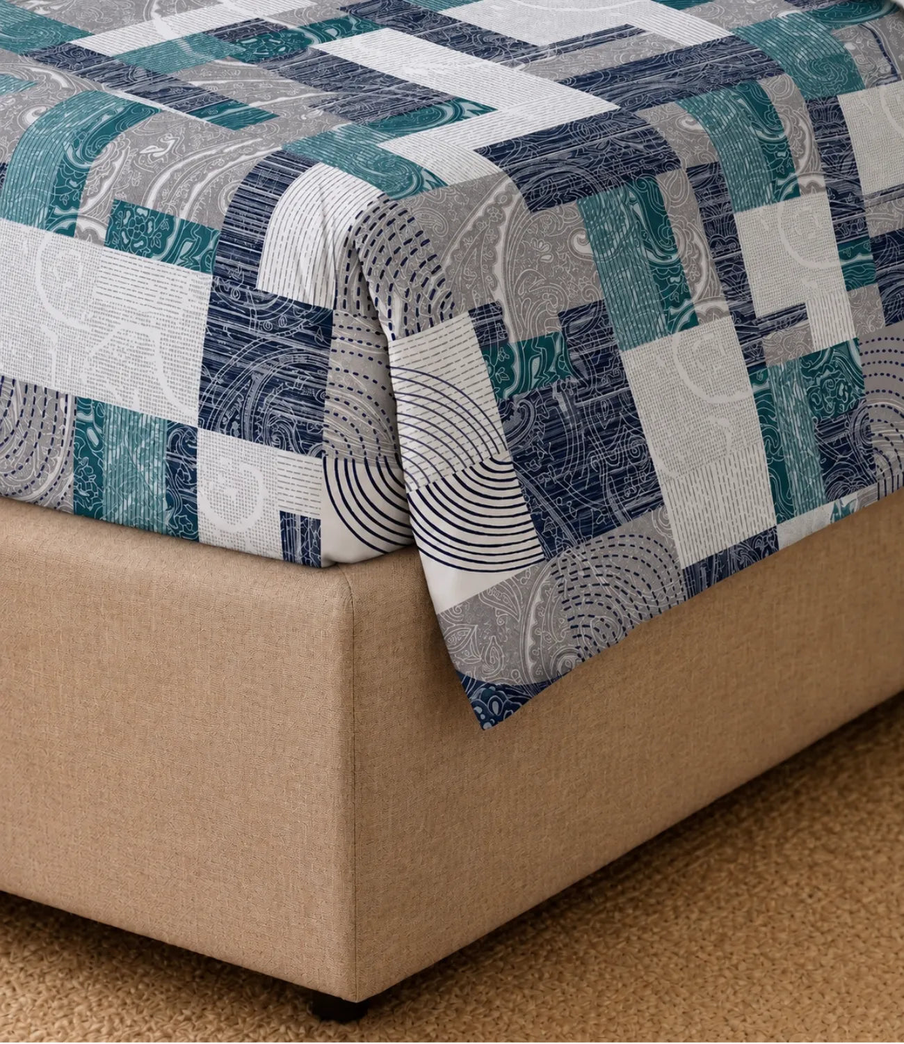 Close-up of a teal geometric patchwork cotton bedsheet draped over a bed corner, highlighting the bold print and smooth fabric finish.